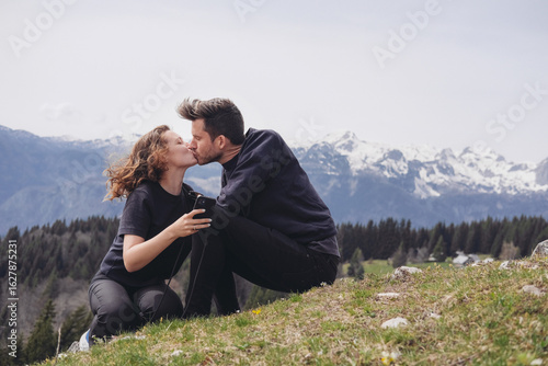 Wallpaper Mural A young couple - a woman and a man kissing, sitting on the grass in the mountians  Torontodigital.ca
