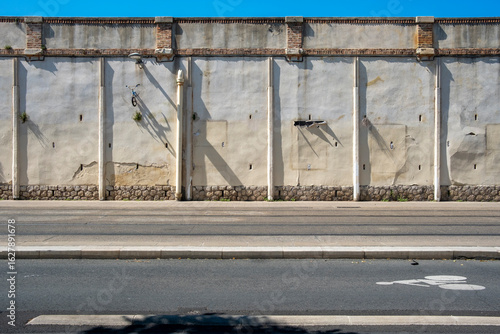 Concrete wall along city road with shadow play and urban texture, ideal for themes around urban barriers, planning, silence, limits, resilience and graphic branding in infrastructure.