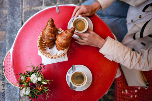 Tableau sur toile Overhead shot of two people enjoying croissants and coffee at outdoor cafe table