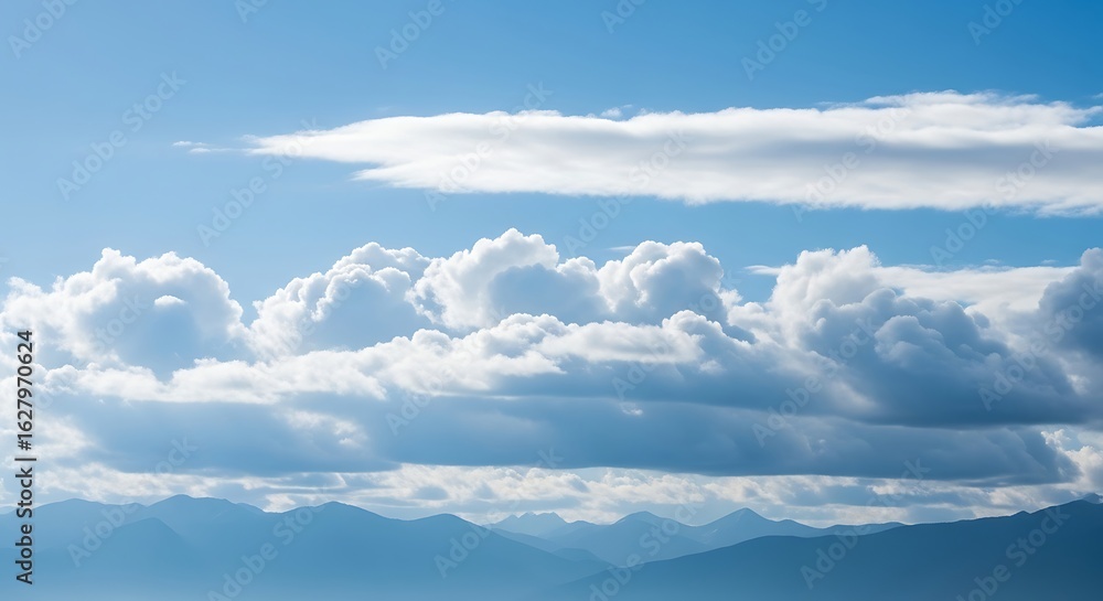 Fototapeta premium Serene mountain range beneath a calming blue sky dotted with fluffy clouds