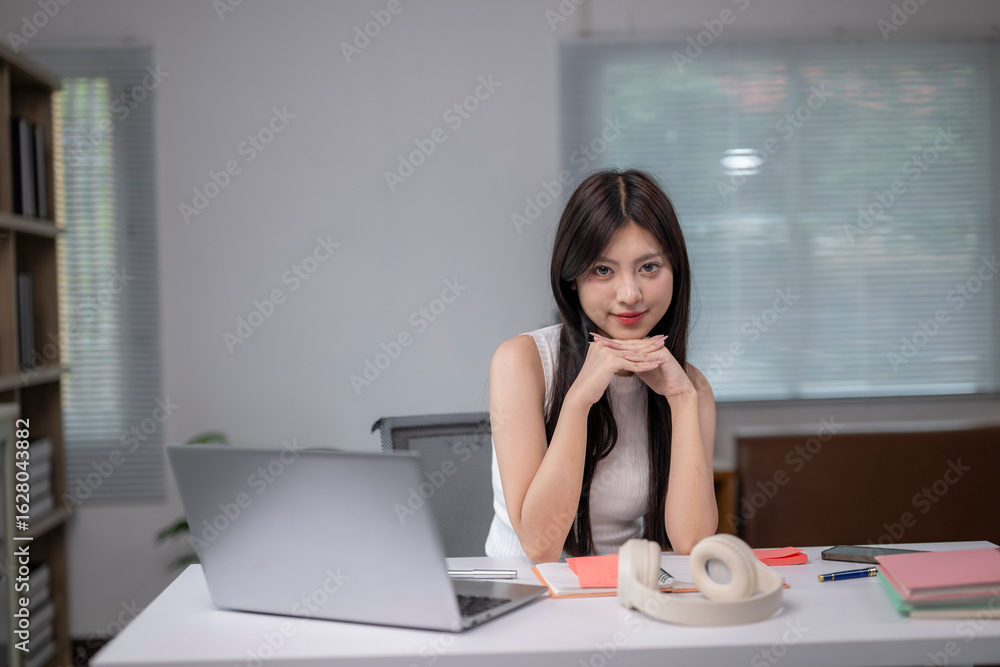 Obraz premium A woman is sitting at a desk with a laptop and a pair of headphones