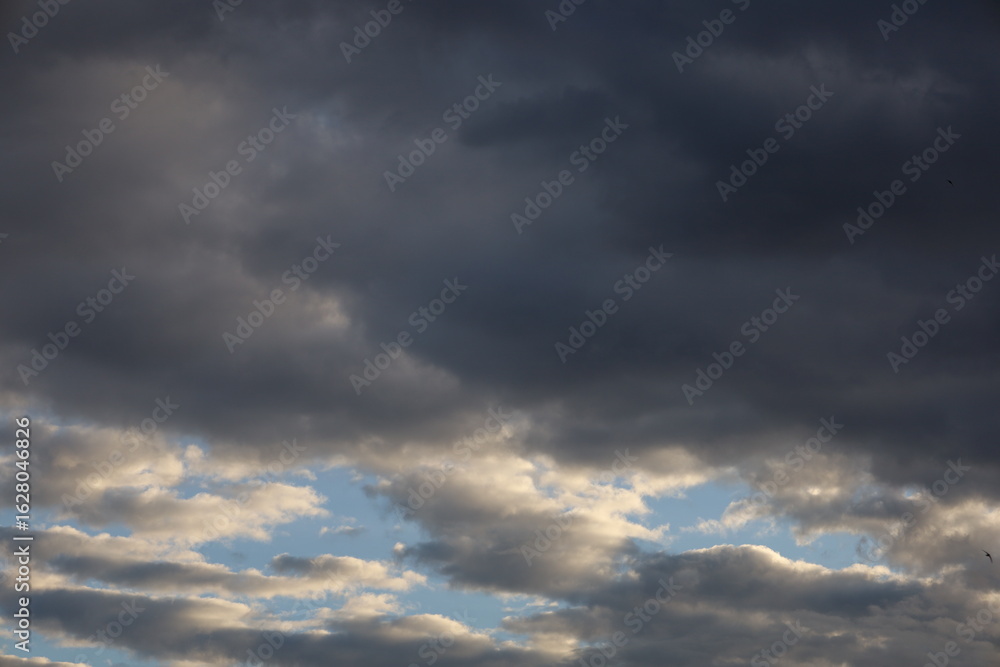 Fototapeta premium Dramatic timelapse of dark storm clouds rolling across a turbulent blue sky at sunset