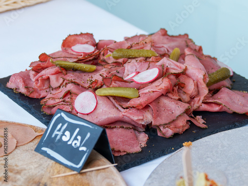 Tranches de pastrami halal avec cornichons et radis, présentées sur un plateau de service

