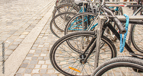 Row of bicycles locked at a bike rack on a cobblestone street in a European city.