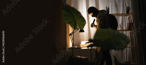 Burglar or intruder with flashlight. Illegally breaking. Male robber wearing black balaclava steals money from apartment. Thief committing theft. Criminal offence. burglary and housebreaking