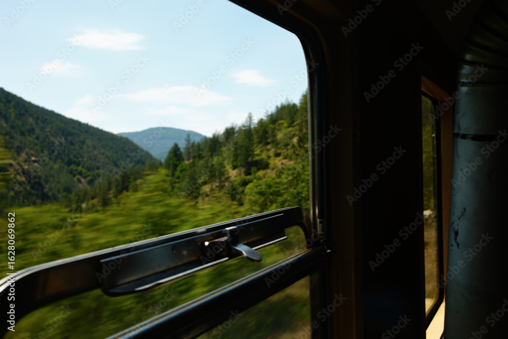 Fototapeta premium Scenic view through an open train window in Mokra Gora, Serbia, with forested hills and blue sky.