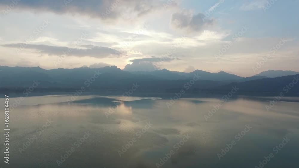 A tranquil lake reflects the majestic mountains under a cloudy sky at sunrise A tranquil lake reflects the majestic mountains under a cloudy sky at sunrise