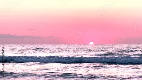 Peaceful sea waves under a pastel pink sunrise sky with the sun touching the horizon. Ideal for meditation videos, travel content, nature backgrounds, or romantic visual themes