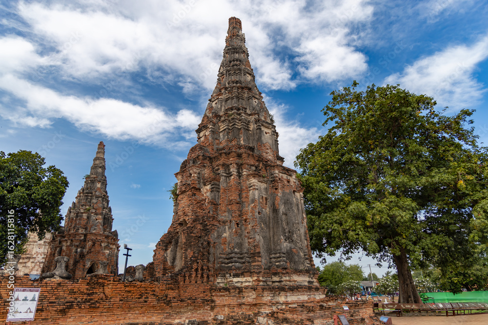 Fototapeta premium Historic brick temple tower at Wat Chaiwatthanaram in Ayutthaya surrounded by trees and cloudy sky