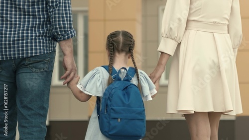 little girl goes hand in hand with parents to school, kid with a backpack on his back, teaching in elementary school, teaching knowledge of the school educational program, happy family.