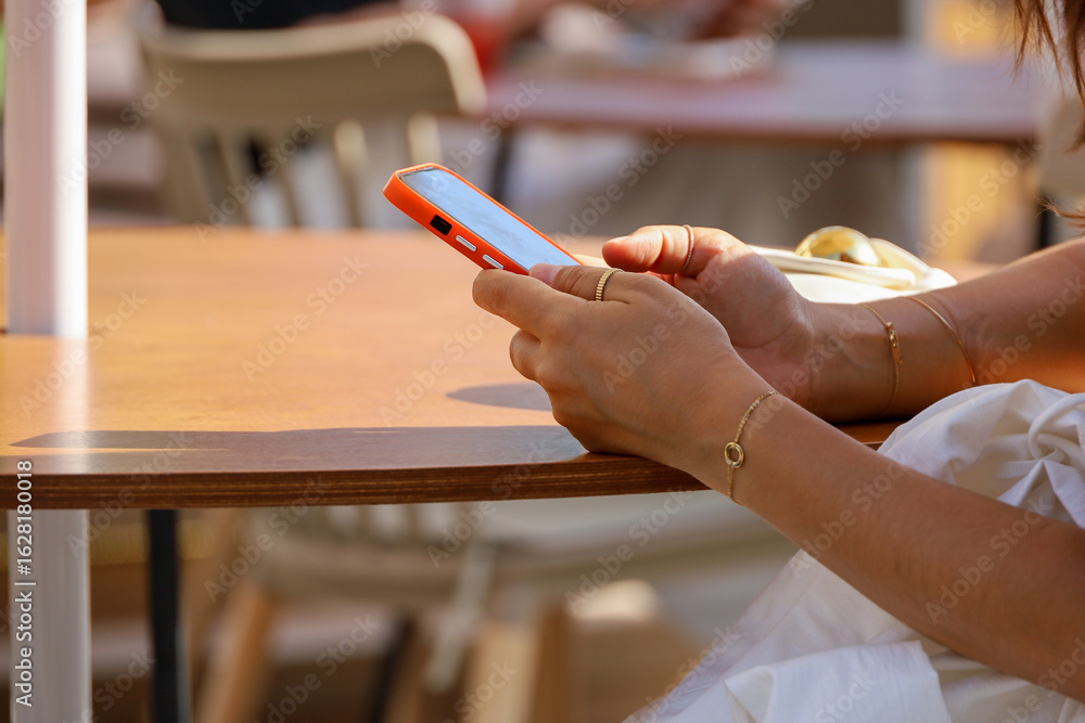 Obraz premium Smartphone in female hand on a street. Woman using mobile phone sitting at the cafe table in summer city