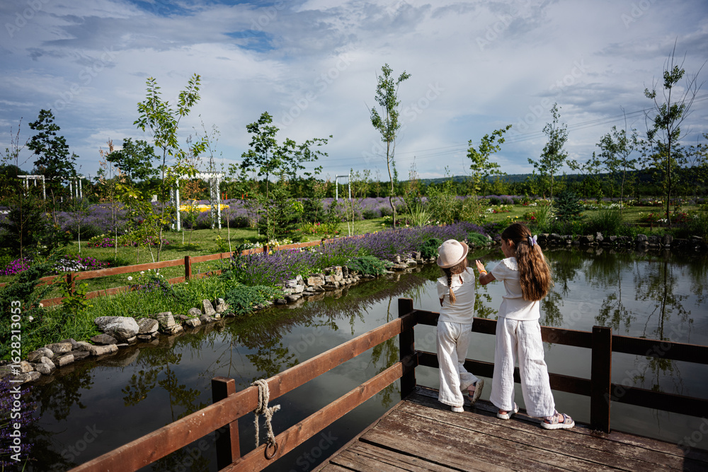 Fototapeta premium Two young girls enjoying a tranquil park by a beautiful pond