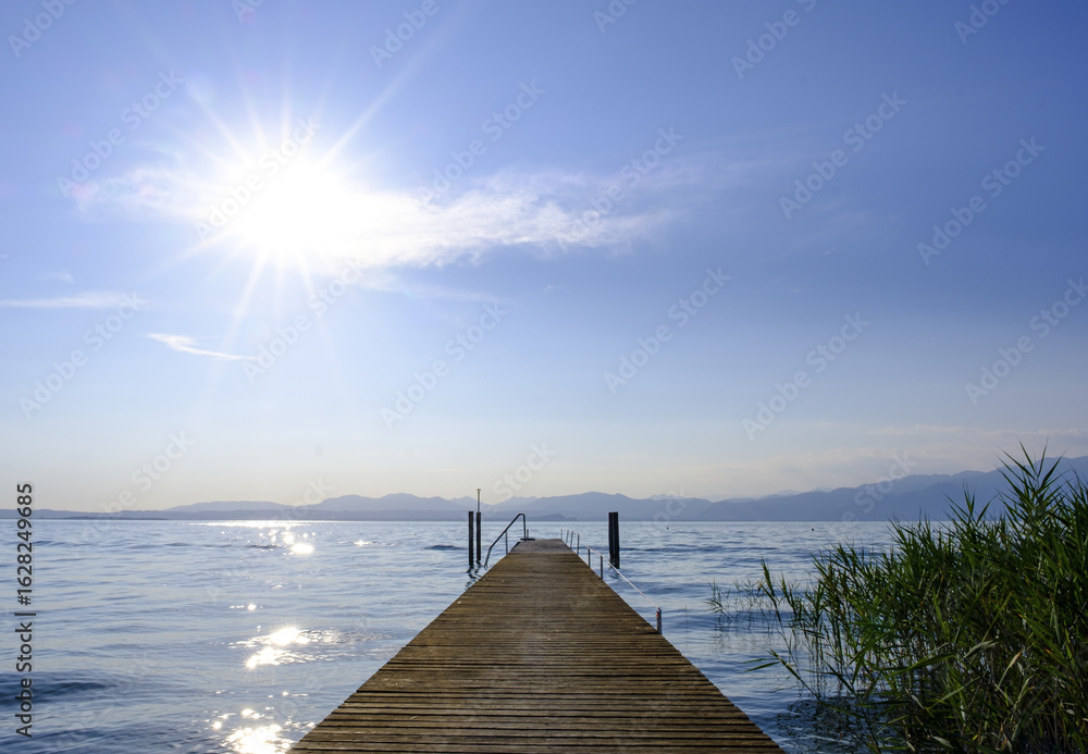 Obraz premium The sunset over Lake Garda paints the sky, seen from a pier, creating an unforgettable postcard view, Italy.