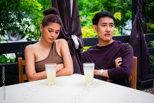 Photography Frustrated young Asian couple avoid eye contact during a failed date at an alfresco cafe