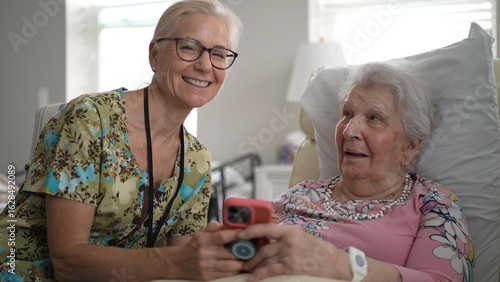 Φωτογραφία Portrait of nurse while sharing memories and information with an elderly woman in her senior living room, using a smartphone to connect and enhance their visit experience