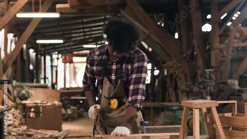 Young African American Carpenter Using Hand Saw To Cut Wood Crafting Handmade Furniture In Workshop Demonstrating Skill And Precision