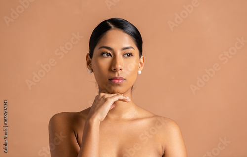 Thoughtful young woman touching chin posing on beige background