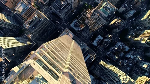 Bird's-eye view of a tall skyscraper looking down on a dense city during daytime, shadows cast on other buildings