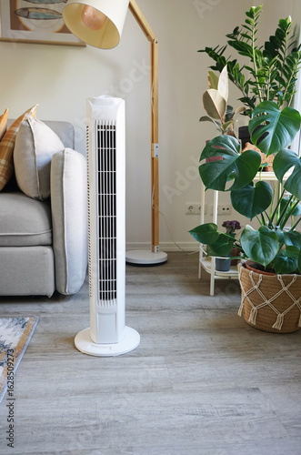 White tower fan against background of flowers and sofa in modern light interior