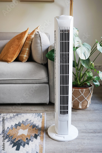 White tower fan against background of flowers and sofa in modern light interior