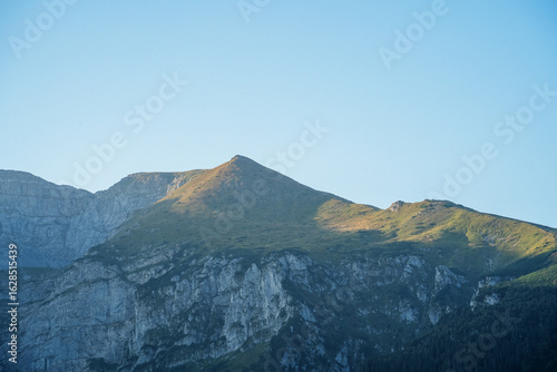 Fototapeta Naklejka Na Ścianę i Meble -  The warm light of the sun illuminates the smooth, grassy summit of a mountain set against its rugged, rocky base. Picture taken on a holiday trip to Zakopane, Poland with my Sony a7III