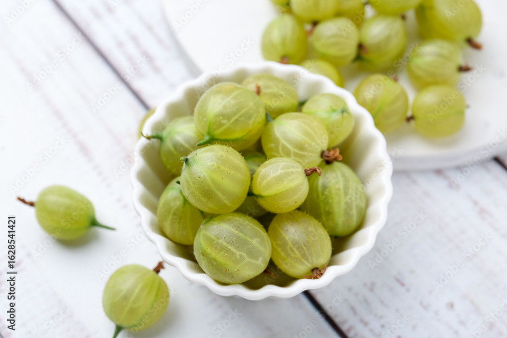 Fresh green gooseberries in bowl on white wooden table, above view Fresh green gooseberries in bowl on white wooden table, above view
