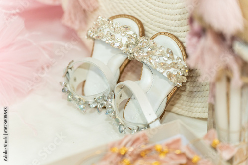 Elegant children's sandals adorned with sparkling embellishments set against a soft pastel background on a pillow