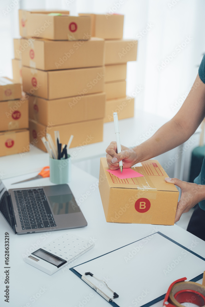 Fototapeta premium Package Preparation: A person meticulously prepares packages for shipment on a well-organized desk, with stacks of parcels and office supplies, readying orders for delivery. 