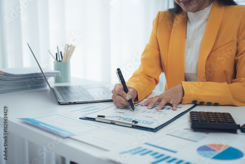 The Art of Precision: An accountant meticulously reviews financial documents in a well-lit office. Pen poised above the paperwork, she is a picture of focus, a professional deeply engaged in her work.