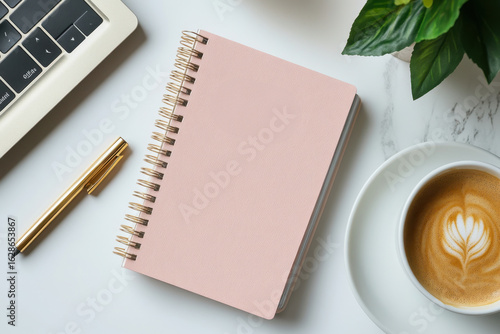 Pink notebook, pen, and coffee on white table.