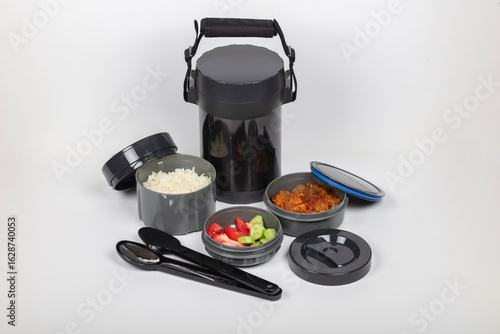 Stainless steel insulated lunch box container set with compartments filled with rice, meat eggplant dish, vegetables on white background food storage