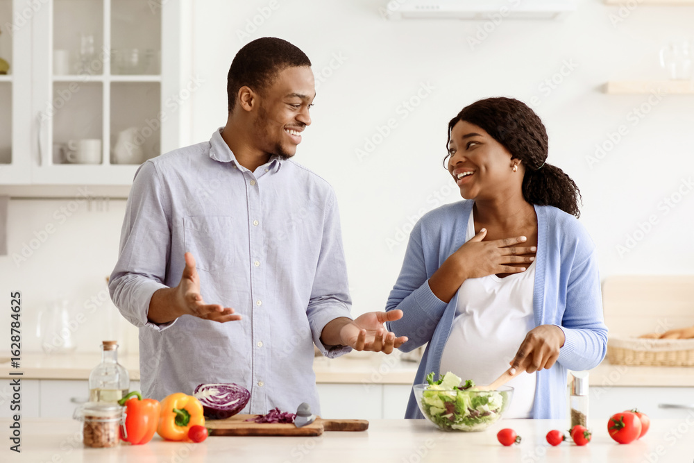 Happy young pregnant black family husband and wife having fun while cooking vegetable salad together, having conversation and laughing, kitchen interior, copy space. Healthy lifestyle during pregnancy Happy young pregnant black family husband and wife having fun while cooking vegetable salad together, having conversation and laughing, kitchen interior, copy space. Healthy lifestyle during pregnancy