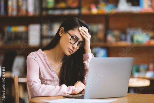 Disappointed arab lady using laptop and having problems, working on computer remotely in cafe, suffering from headache and emotionally reacting to business troubles, free space