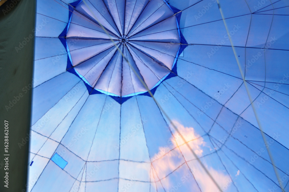 Fototapeta premium View from a hot air balloon basket, looking up at the burner flame heating the blue envelope during flight