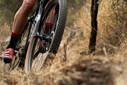 A close-up of a mountain bike in action on rough terrain. The gears and suspension are captured with great clarity, conveying strength, endurance, and adrenaline.