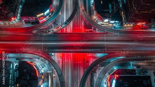Aerial view of a busy highway interchange at night with blurred car light trails in red and white.