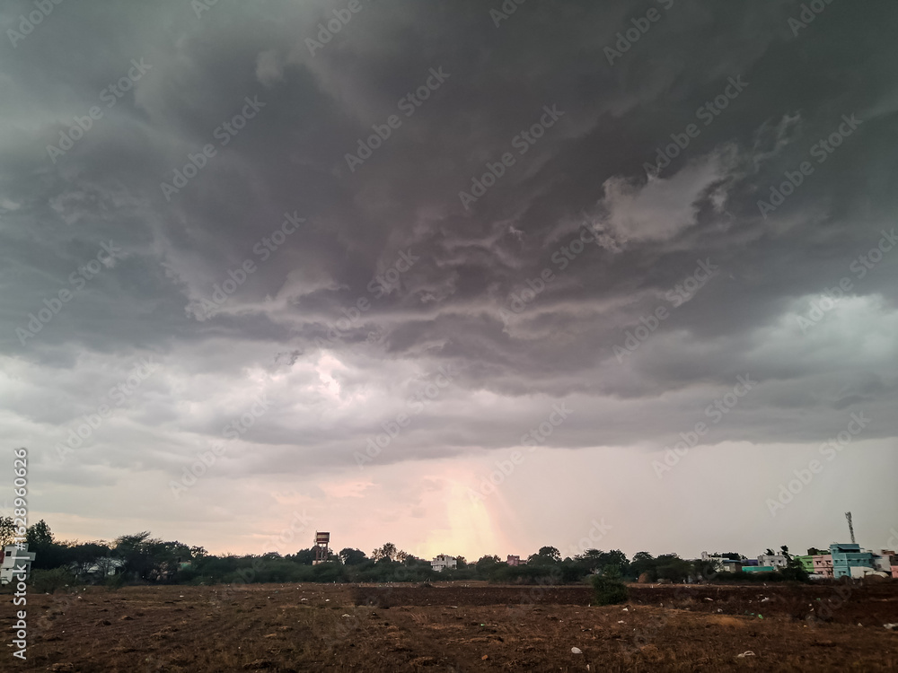 Fototapeta premium Dark Monsoon Clouds Over Rural Landscape with Faint Rainbow Glow