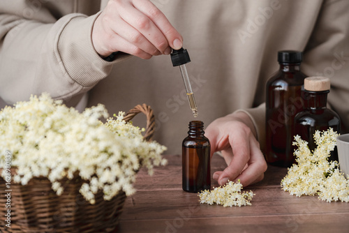 Cuadro en lienzo A person carefully processes elderflower in a cozy workshop, surrounded by dark glass bottles and a basket filled with the vibrant blossoms