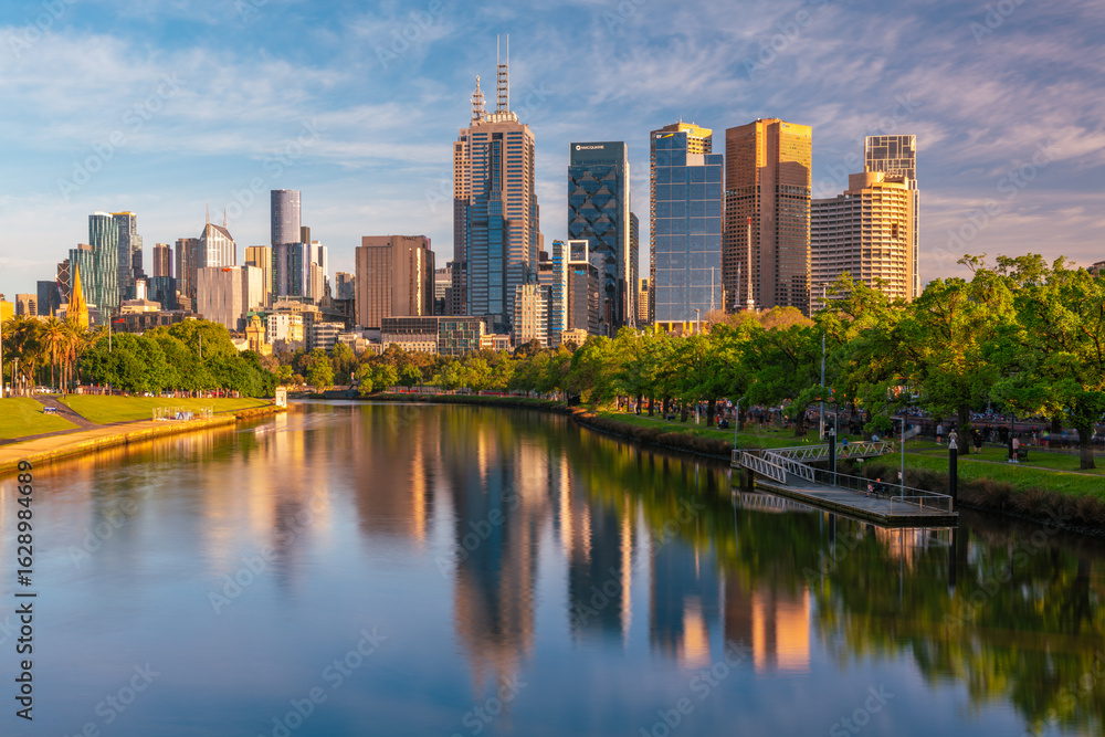 Naklejka premium Early morning view of the city high rise buildings in Melbourne, Victoria, Australia are reflected in the calm water of the Yarra River.