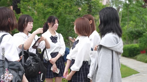 High school girls in uniform gather on a street where trees blend with buildings, chatting and adjusting hair. Shanghai Pudong New District, Zhangjiang Hi-Tech Park Station, spring, real-time video.
