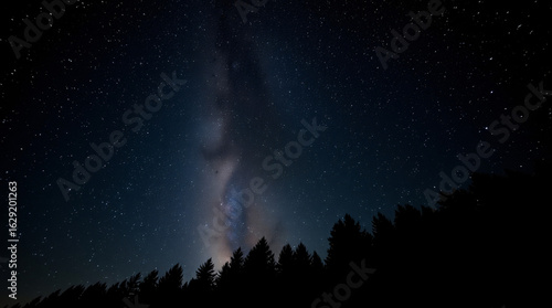 Breathtaking vertical view of the Milky Way glowing brightly above the dark silhouette of a dense forest treeline at night