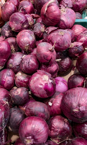 Fresh red onions piled together at a local market, showcasing their rich color and texture under natural lighting in autumn
