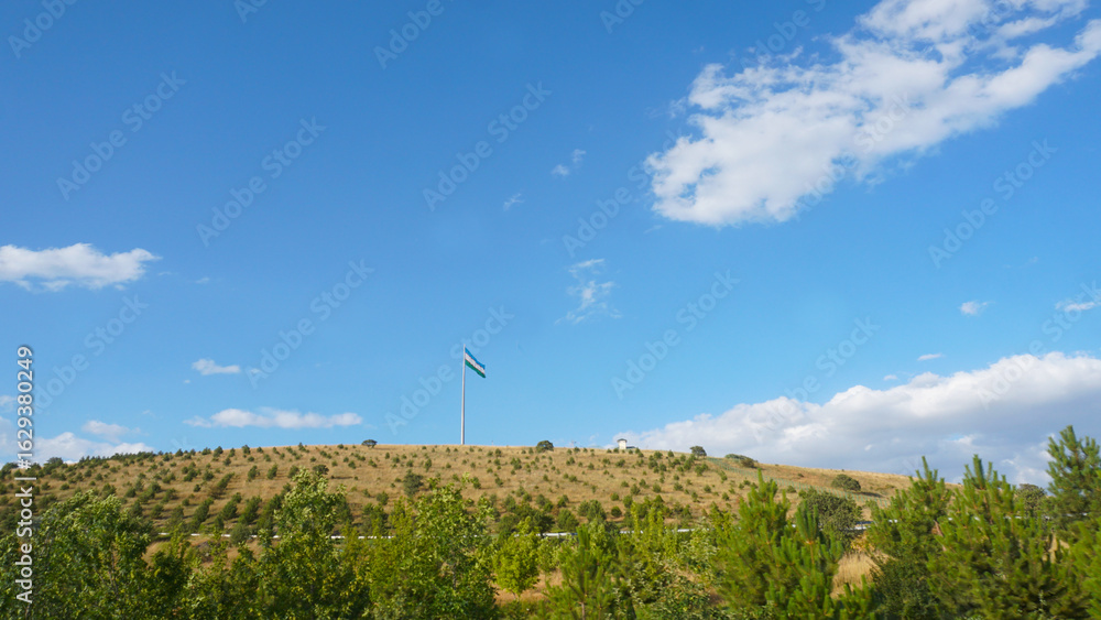 Fototapeta premium The flag of Uzbekistan is visible on a hill in the distance.