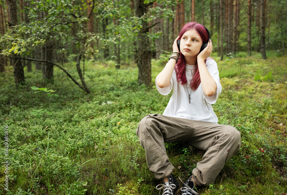 Naklejka premium Young girl listening music with headphones in forest