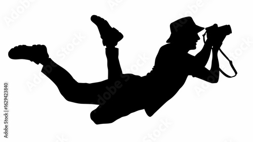 Silhouette of a photographer in a hat lying down taking a picture with a camera in black and white