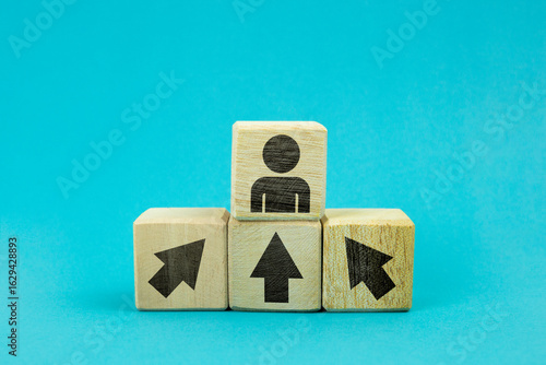 Wooden blocks with arrow stacked like steps leading to a block with a human icon, representing teamwork, leadership, and achieving goals.