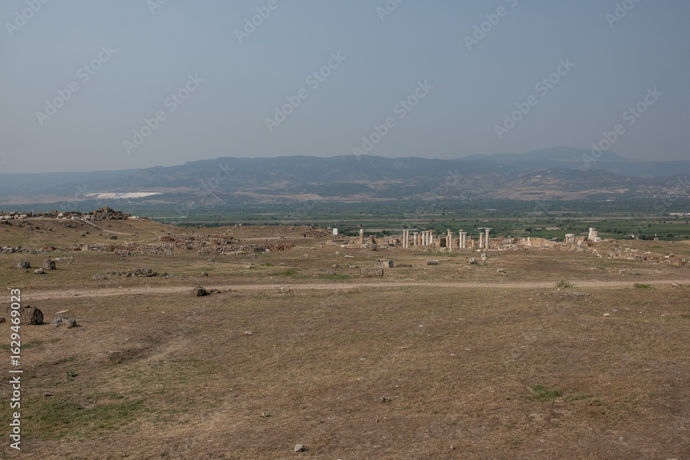 Fototapeta premium Exploration of the extensive ruins of Laodikeia reveals remnants of ancient structures set against a backdrop of rolling hills and open terrain