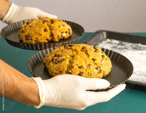 Hands in gloves holding a tray with large homemade chocolate chip cookies
