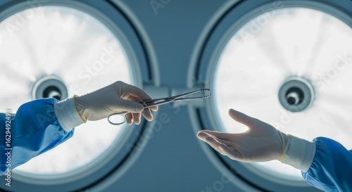 A surgeon's gloved hand passes surgical forceps to another hand under bright operating room lights surgery medical operation hospital healthcare instrument