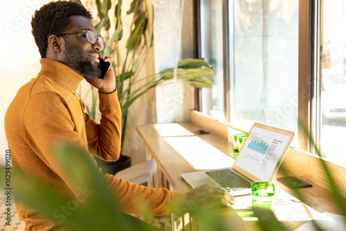 Photos Businessman multitasking at modern workspace speaking on mobile phone and typing